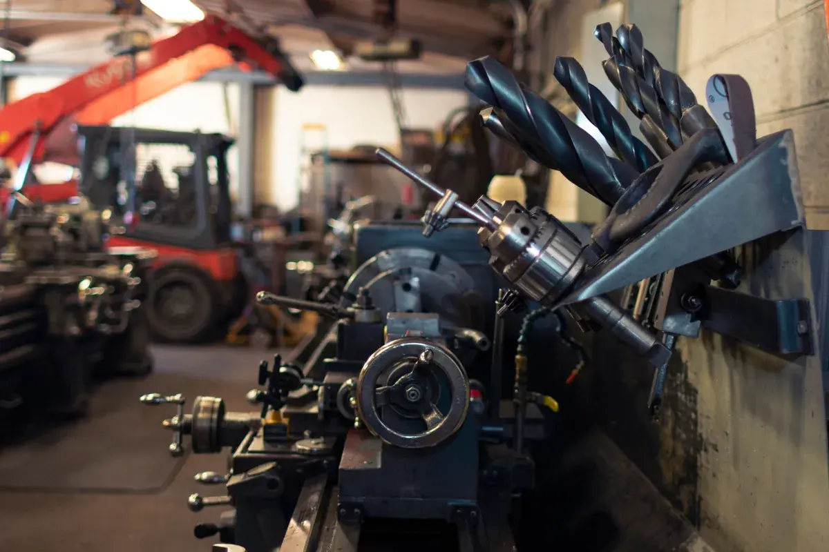 A metal lathe and a rack of drill bits in the foreground of a busy machine shop.