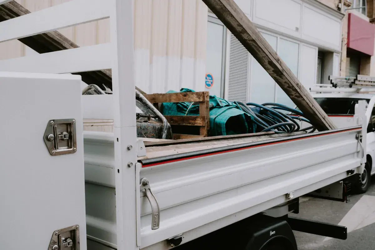An open flatbed work truck parked on a street, loaded with pallets, hoses and building materials.