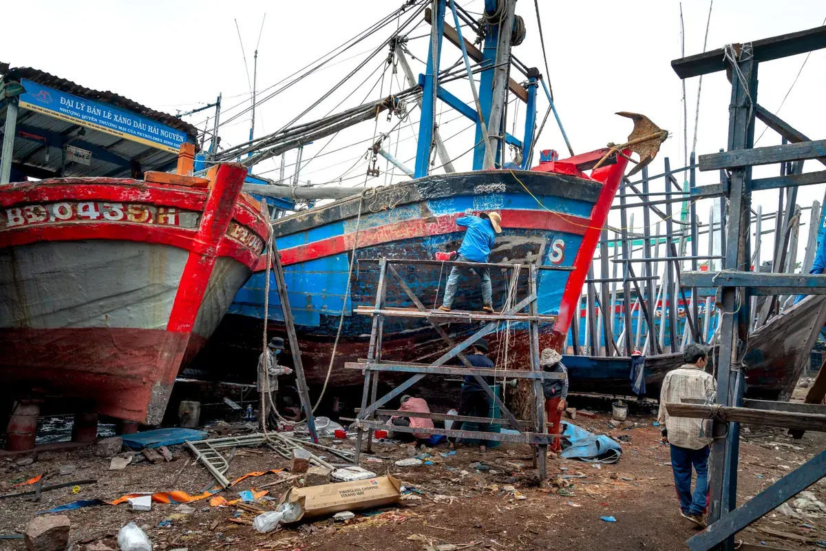 Workers repairing colorful fishing boats in a busy dockyard, focused on the work of the vessel