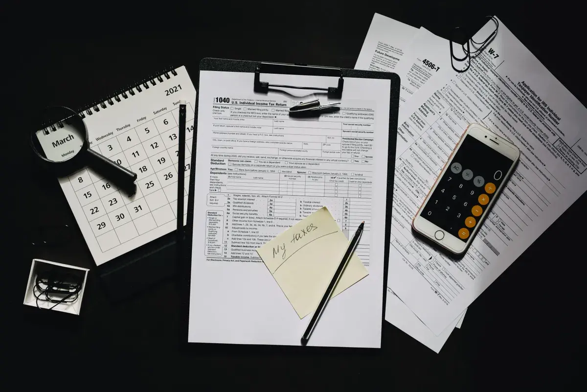 Federal tax forms, a wall calendar, a magnifier and a calculator on a dark desk, arranged as a working file