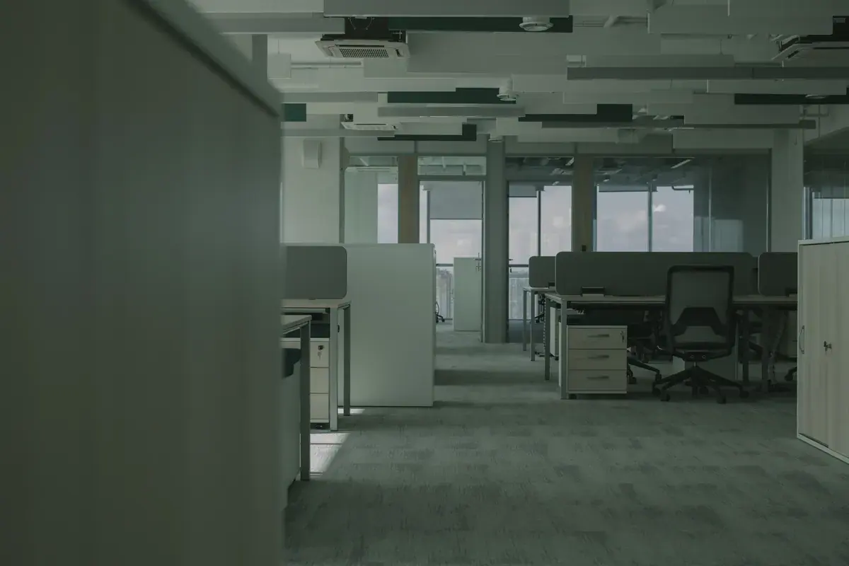 An empty open plan office with dim lighting, rows of desks and partitions after the workday is over