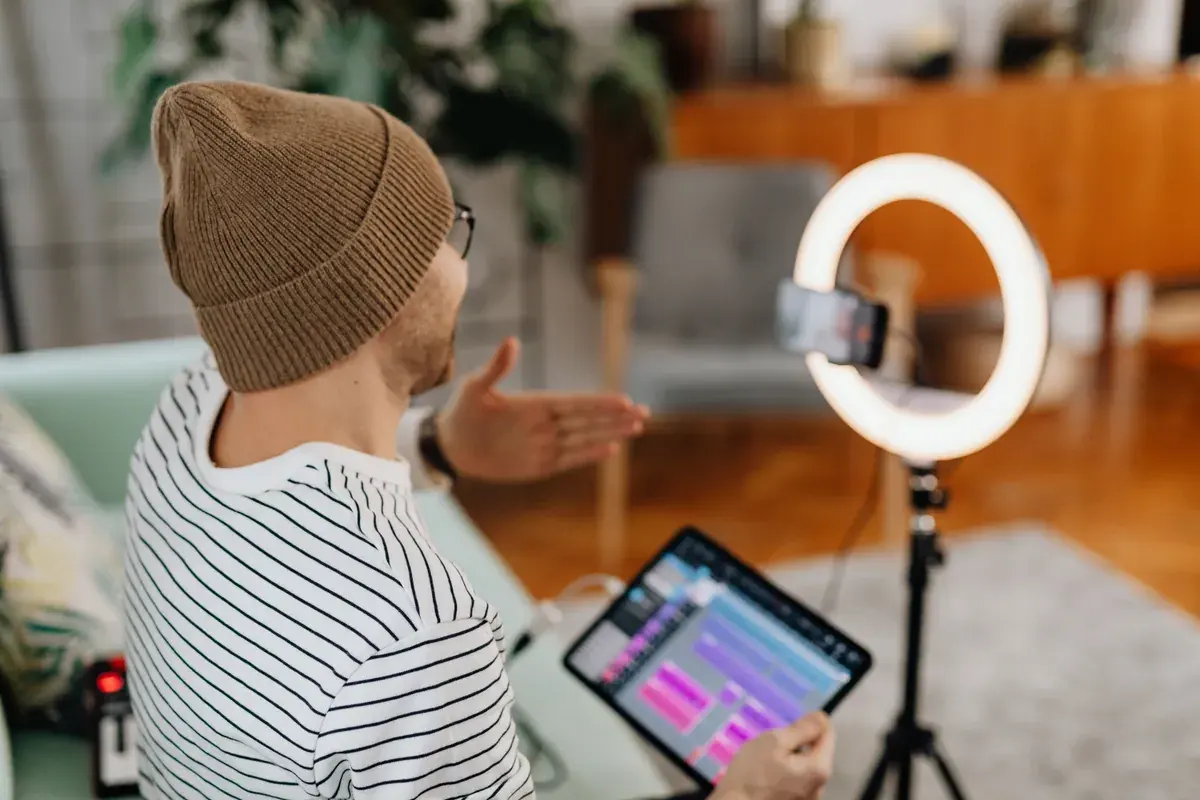 Over the shoulder view of someone recording a video with a phone, ring light and tablet at home.