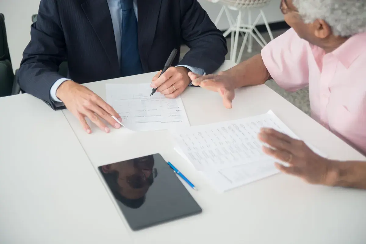 Close-up of two people at a white table comparing printed pages and a blank form.