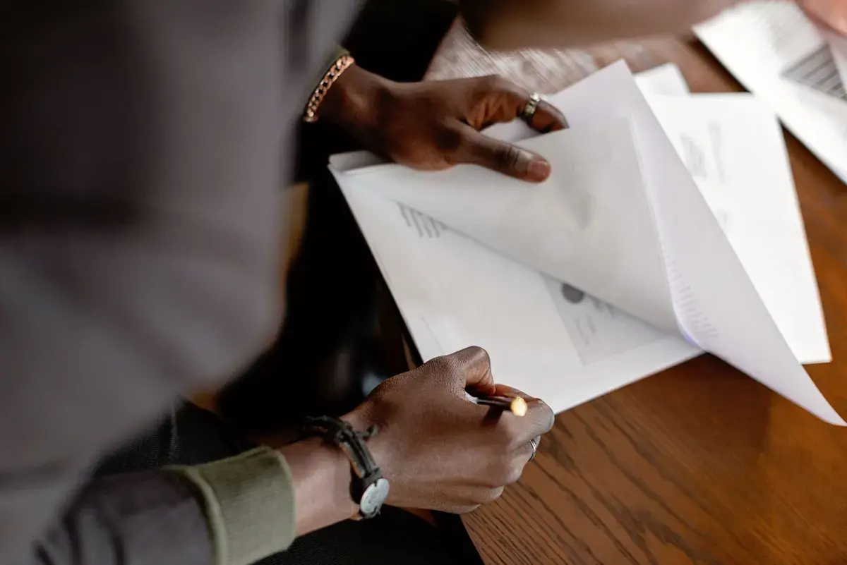 Hands reviewing stapled documents and notes at a wooden desk