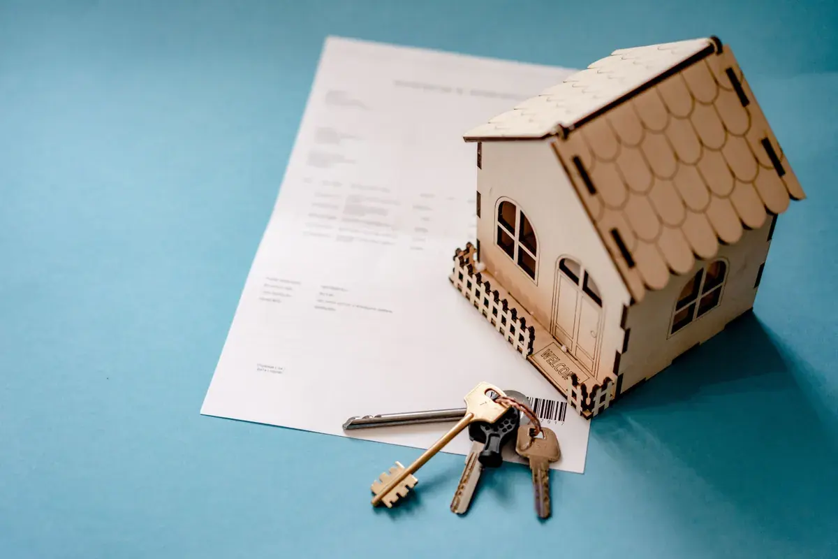 A small wooden house model and a set of keys resting on a printed statement