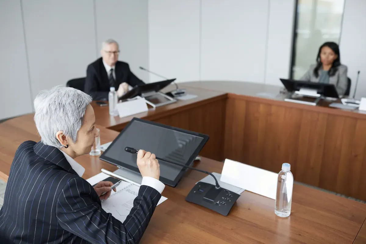 Executives seated around a curved boardroom table with microphones and screens.