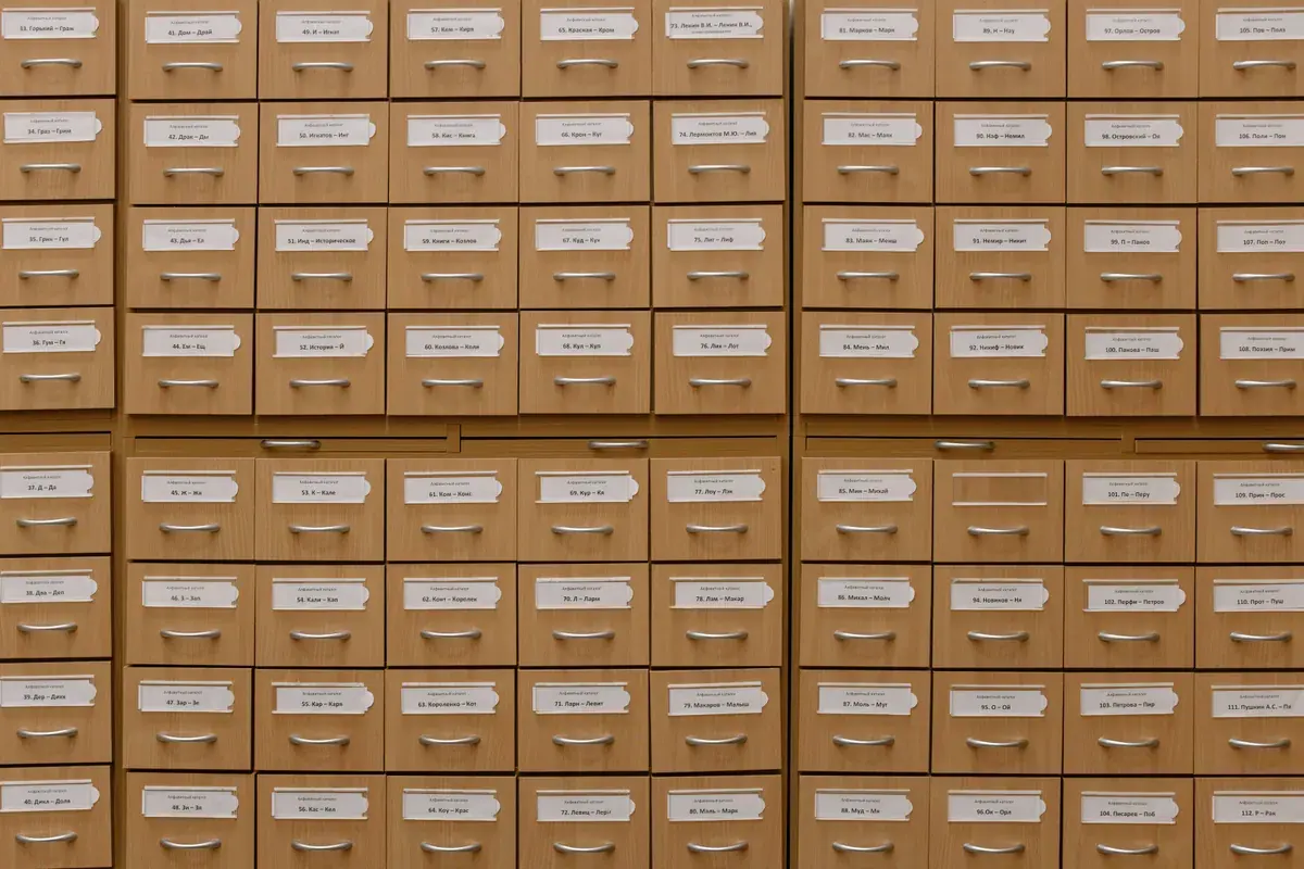 Una pared de cajones de archivo de madera con etiquetas, cada uno con una pequeña ficha de papel.