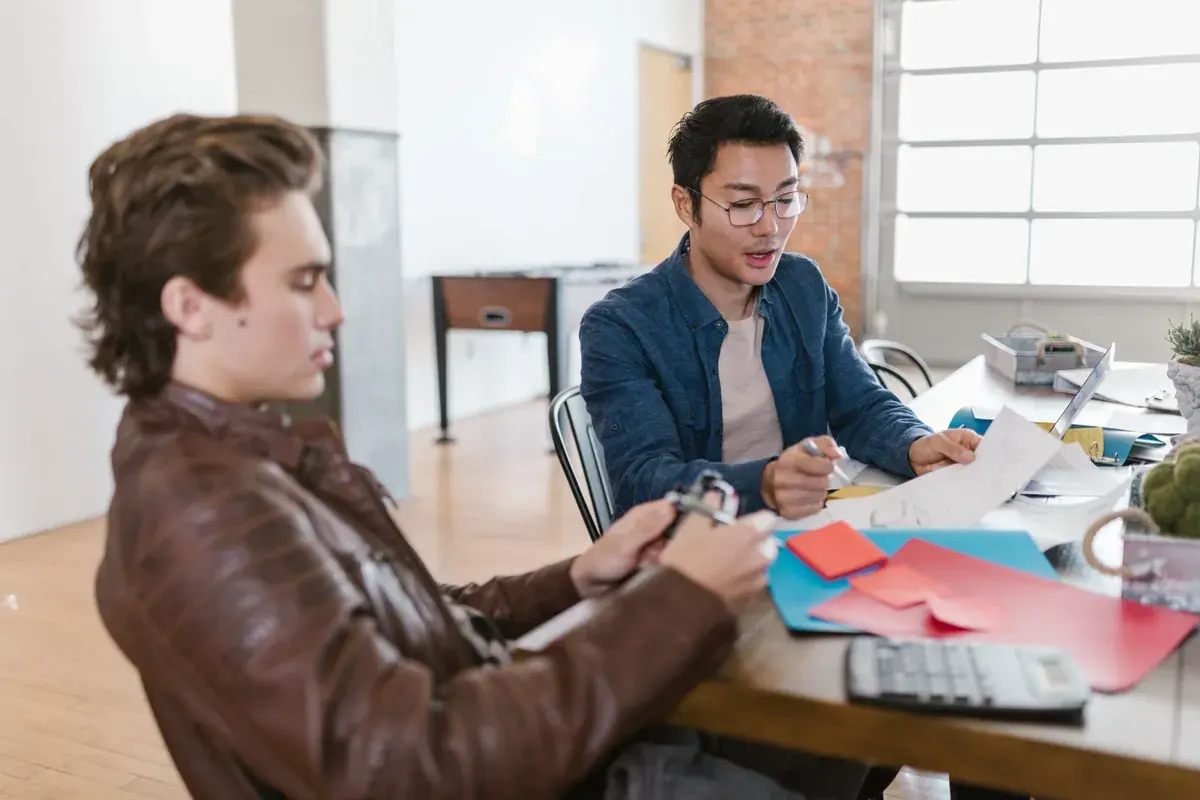 Two founders at a table in a modern office, reviewing sketches and papers together