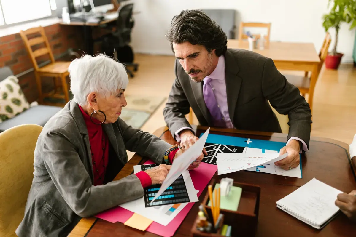 Two colleagues in a warm-lit office reviewing printed charts and documents at a wood table