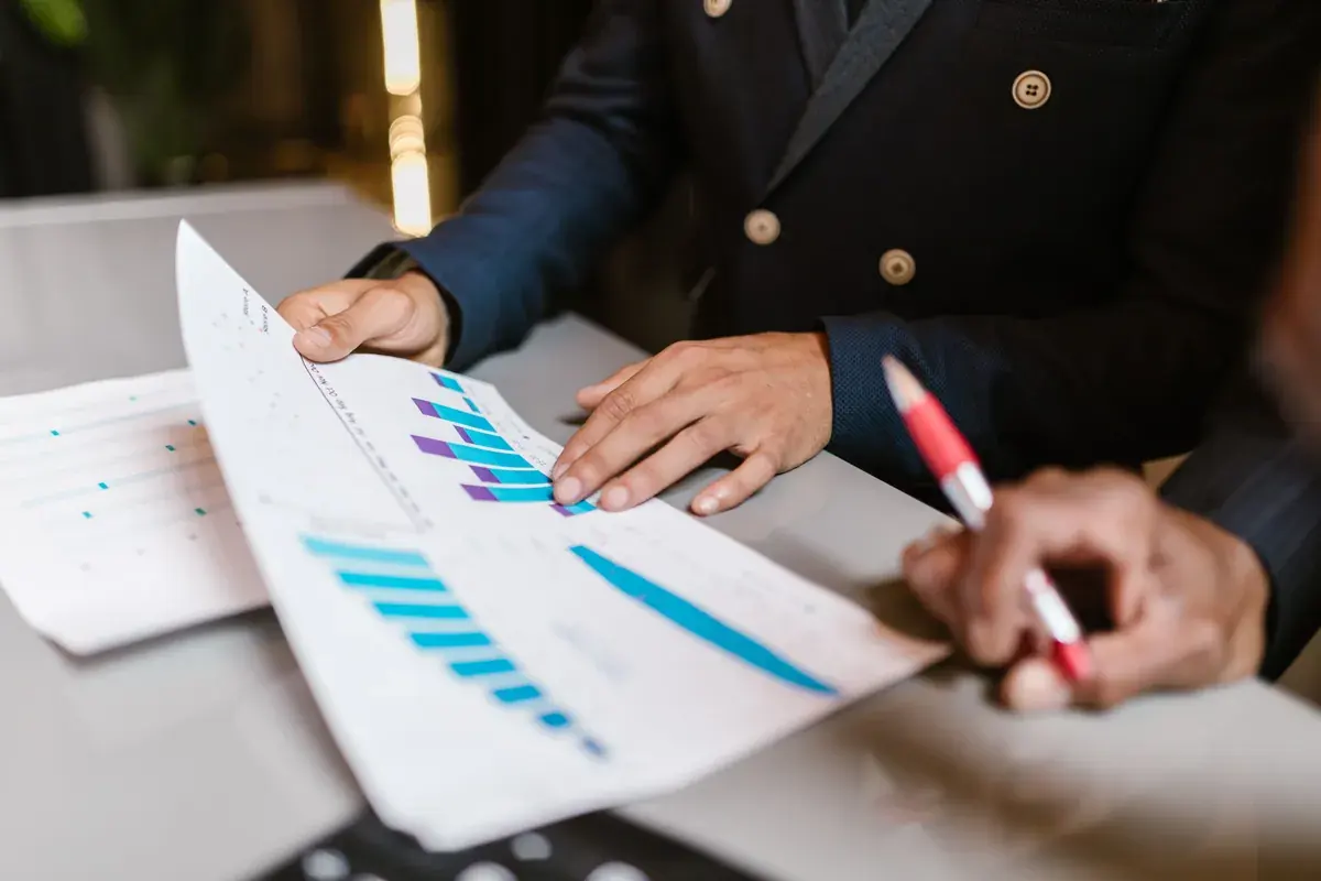 Hands hold printed bar charts above a desk while another person takes notes