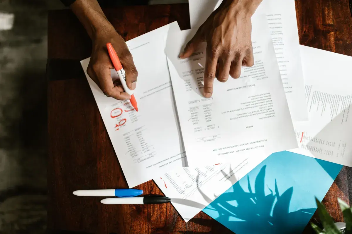 Overhead view of two hands reviewing and marking a printed financial document on a dark wooden desk