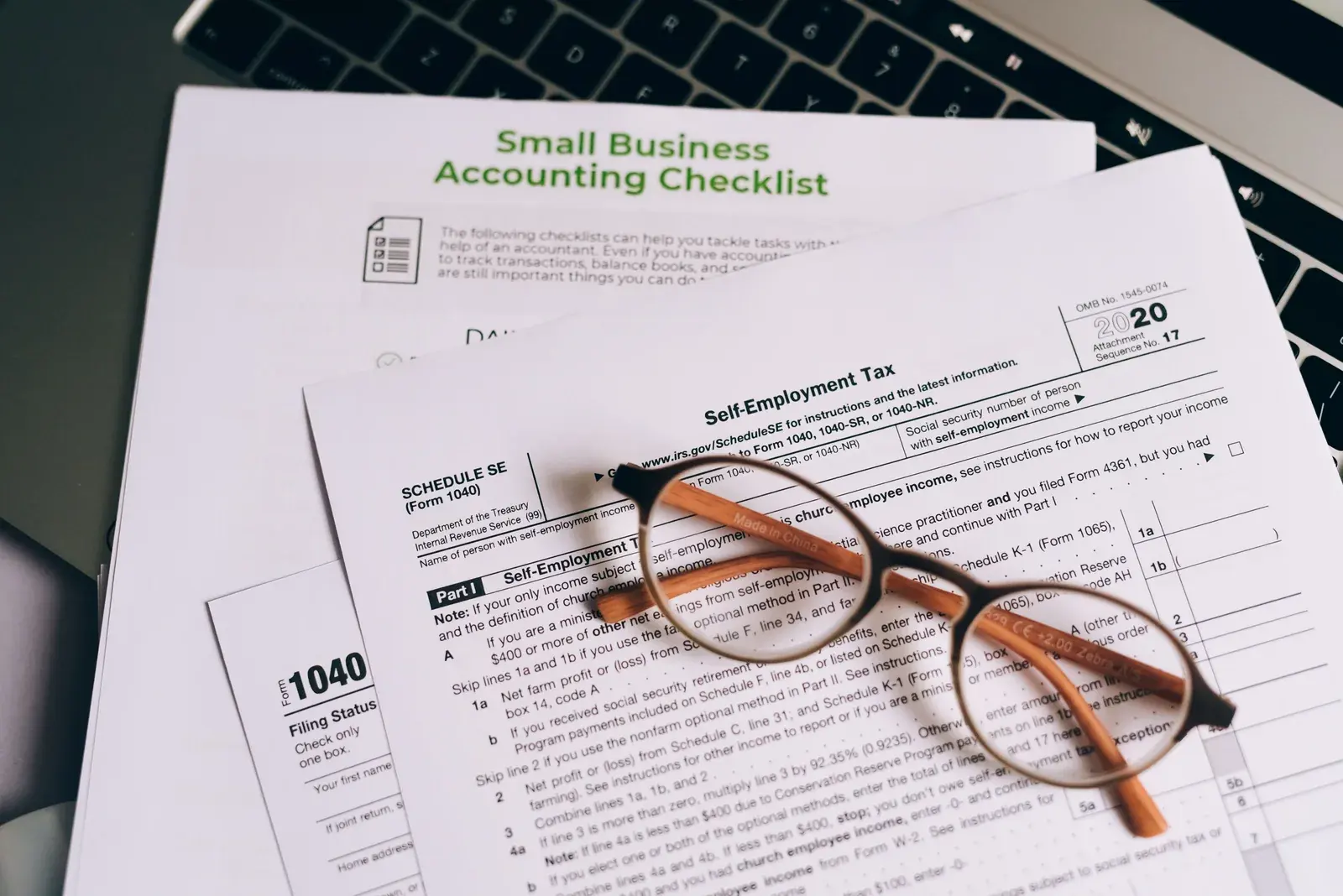 Close-up of a printed small-business accounting checklist and IRS tax forms on top of an open laptop