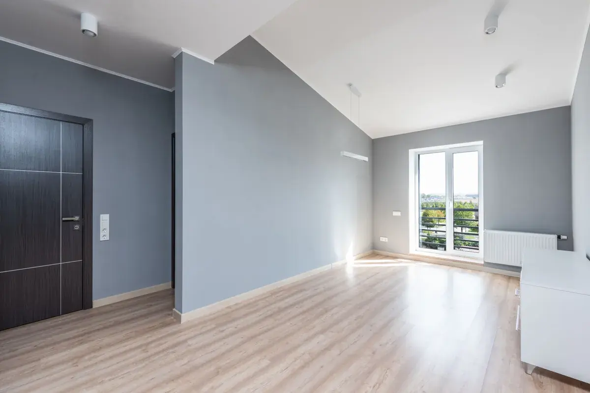 Empty modern room with light wood flooring and a balcony door letting in daylight