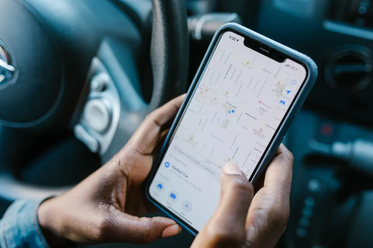 Hands holding a phone showing a route map while seated in a parked car