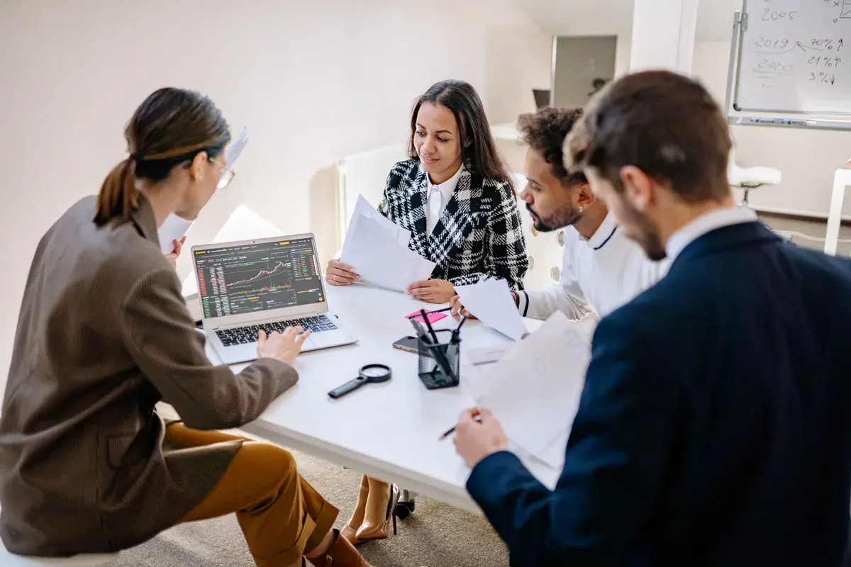 A diverse team analyzing financial data together on a laptop screen in a quiet meeting room