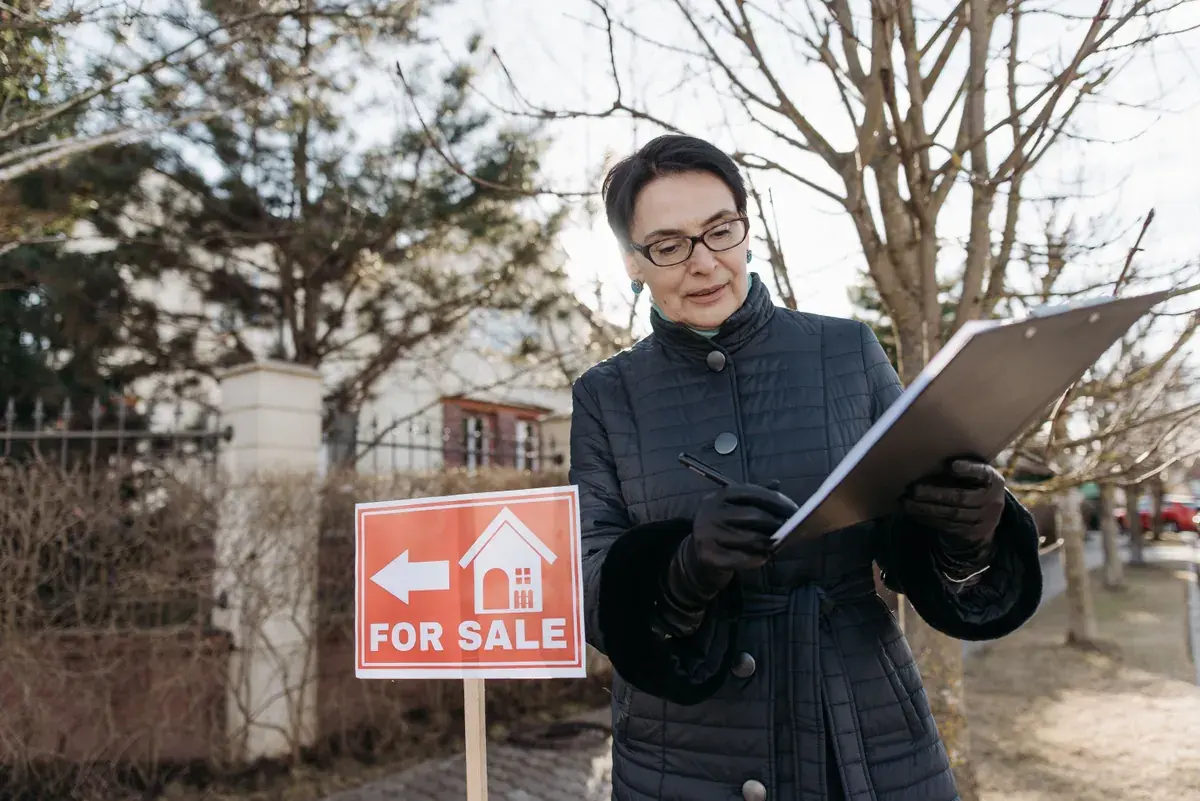A real estate professional reviewing a printed checklist beside a home listing sign