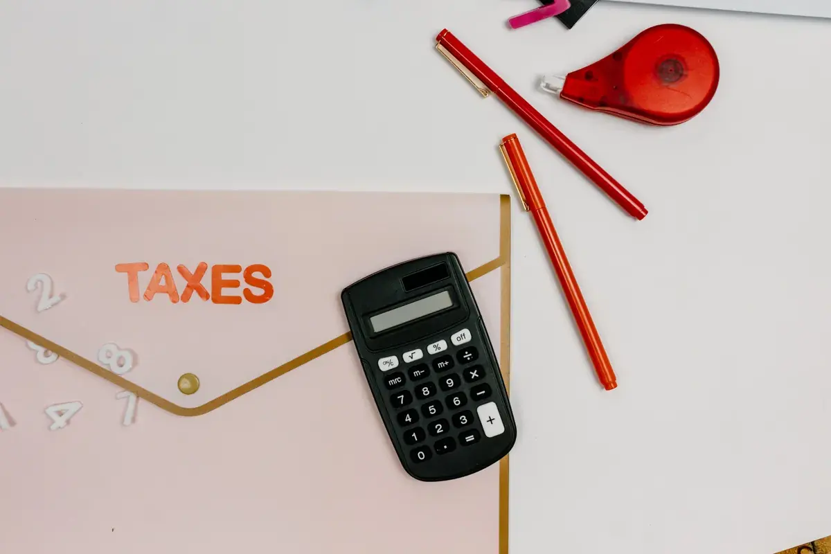 A calculator, a pen, and a folder labeled Taxes resting on a wooden work surface