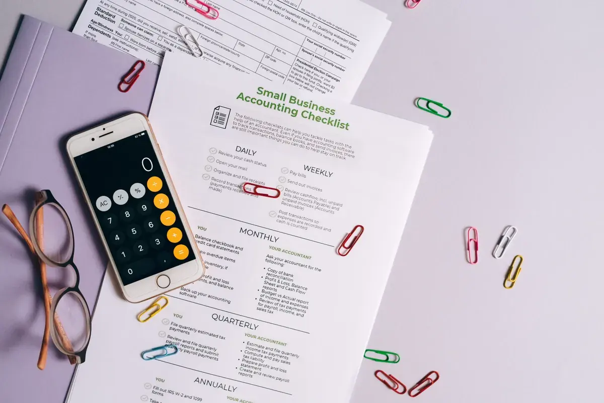 Una vista cenital ordenada de elementos de contabilidad sobre un escritorio de madera con un smartphone, anteojos y papeles impresos