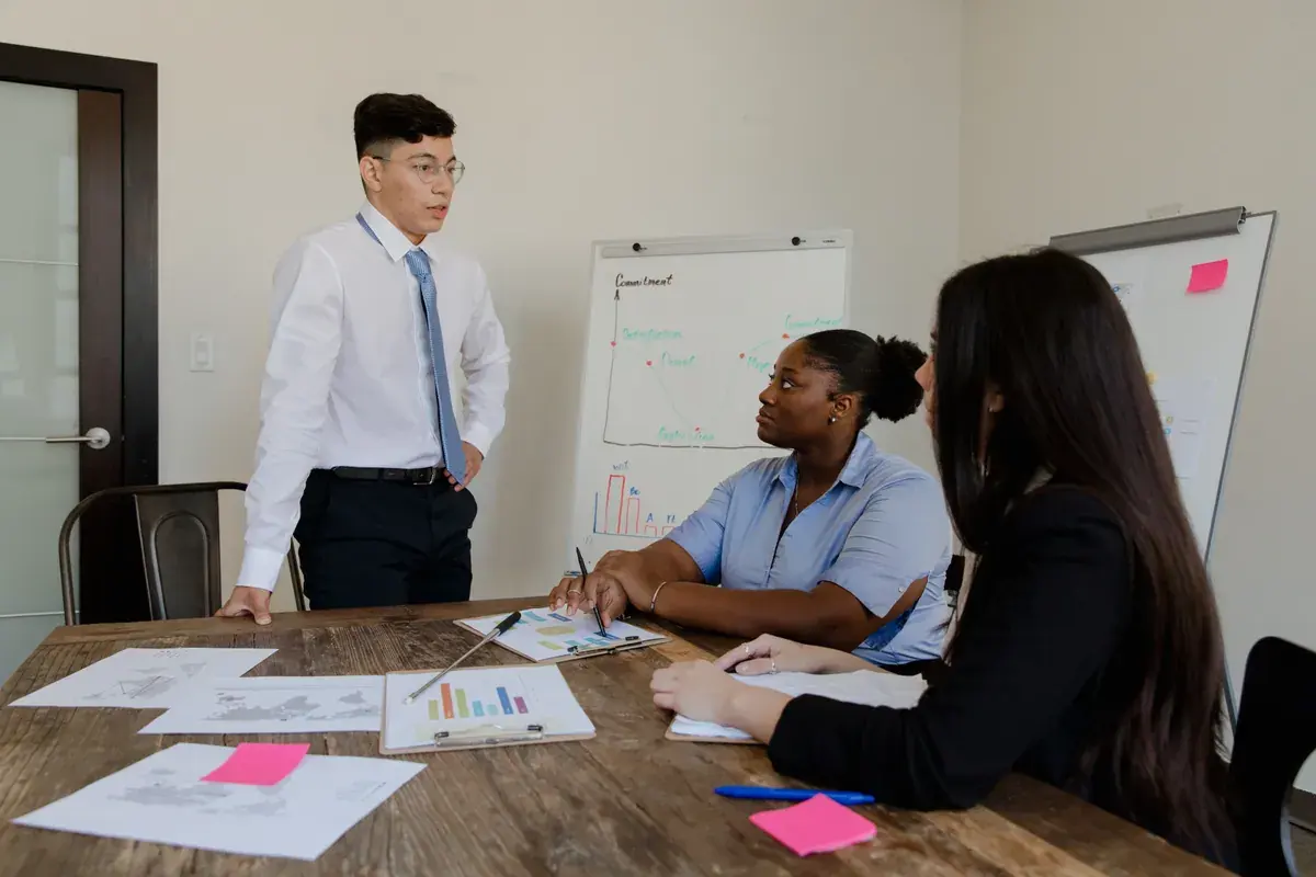 Three diverse professionals at a boardroom table with charts and printed reports