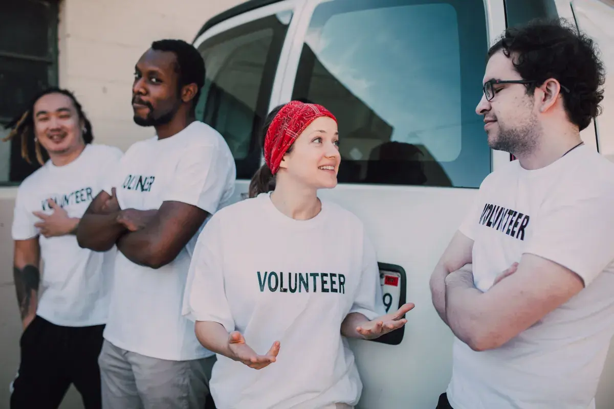 A mixed group of adults in matching shirts standing by a service van at a community event