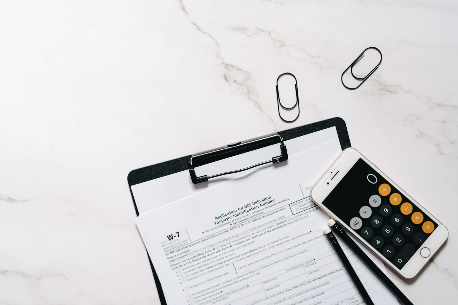 IRS Form W-7, the ITIN application, on a clipboard with a calculator