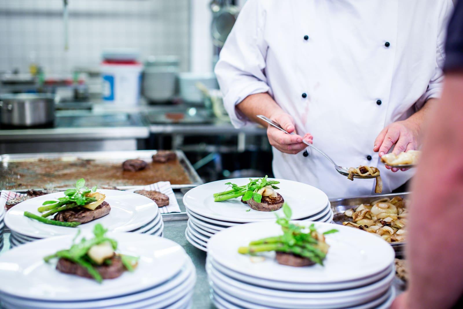 A chef plating dishes on a restaurant kitchen line.