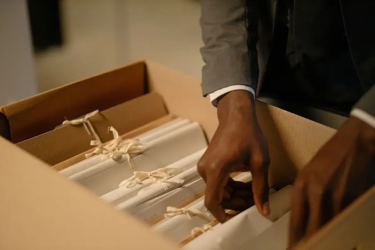 Hands lift a tied bundle of papers from an upright file box.