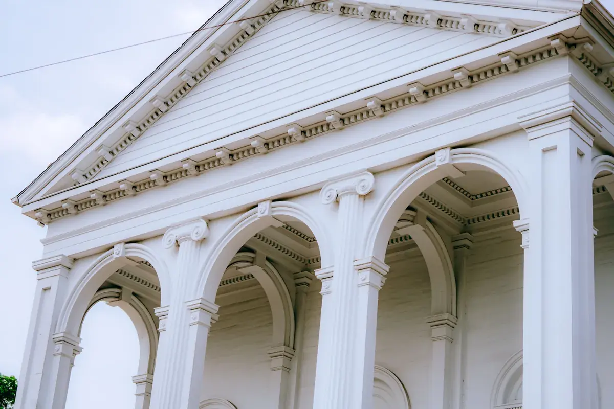 Un edificio gubernamental neoclásico blanco con columnas altas y arcos, visto desde abajo.