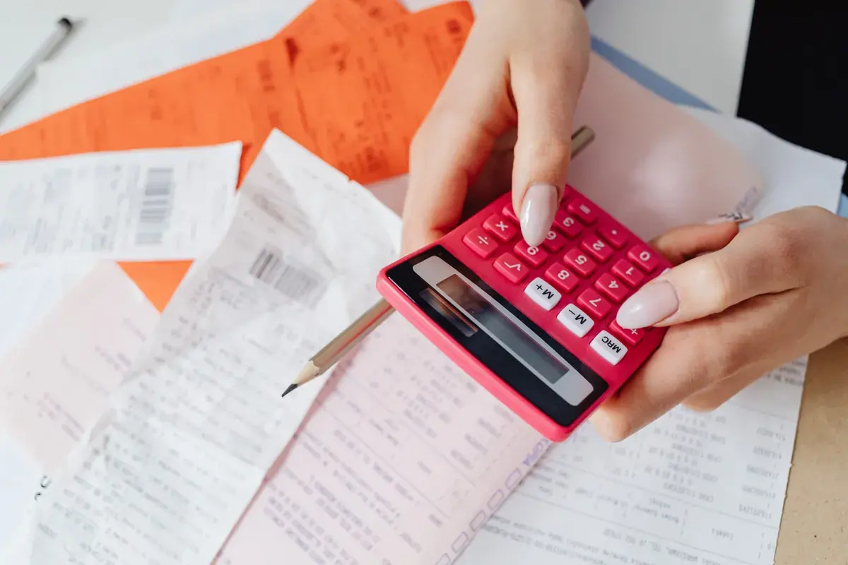 Hands with a calculator working through a fan of paper receipts and slips across a desktop
