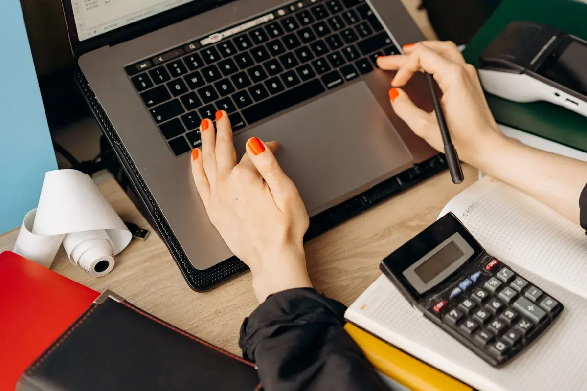 Hands on a laptop keyboard with a calculator sitting alongside on a wooden desk