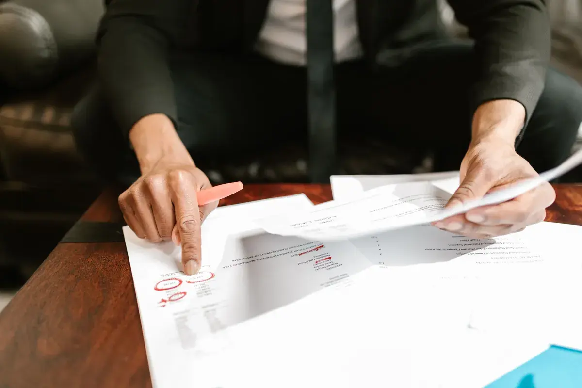 Hands point to circled lines on a printed statement spread across a wooden table.