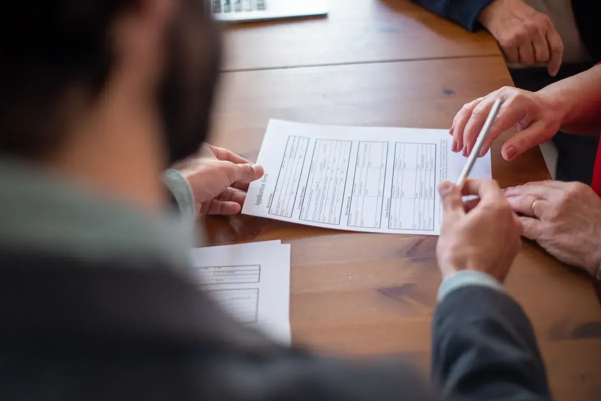 Hands of two people reviewing a printed form together across a wooden table, one holding a pen