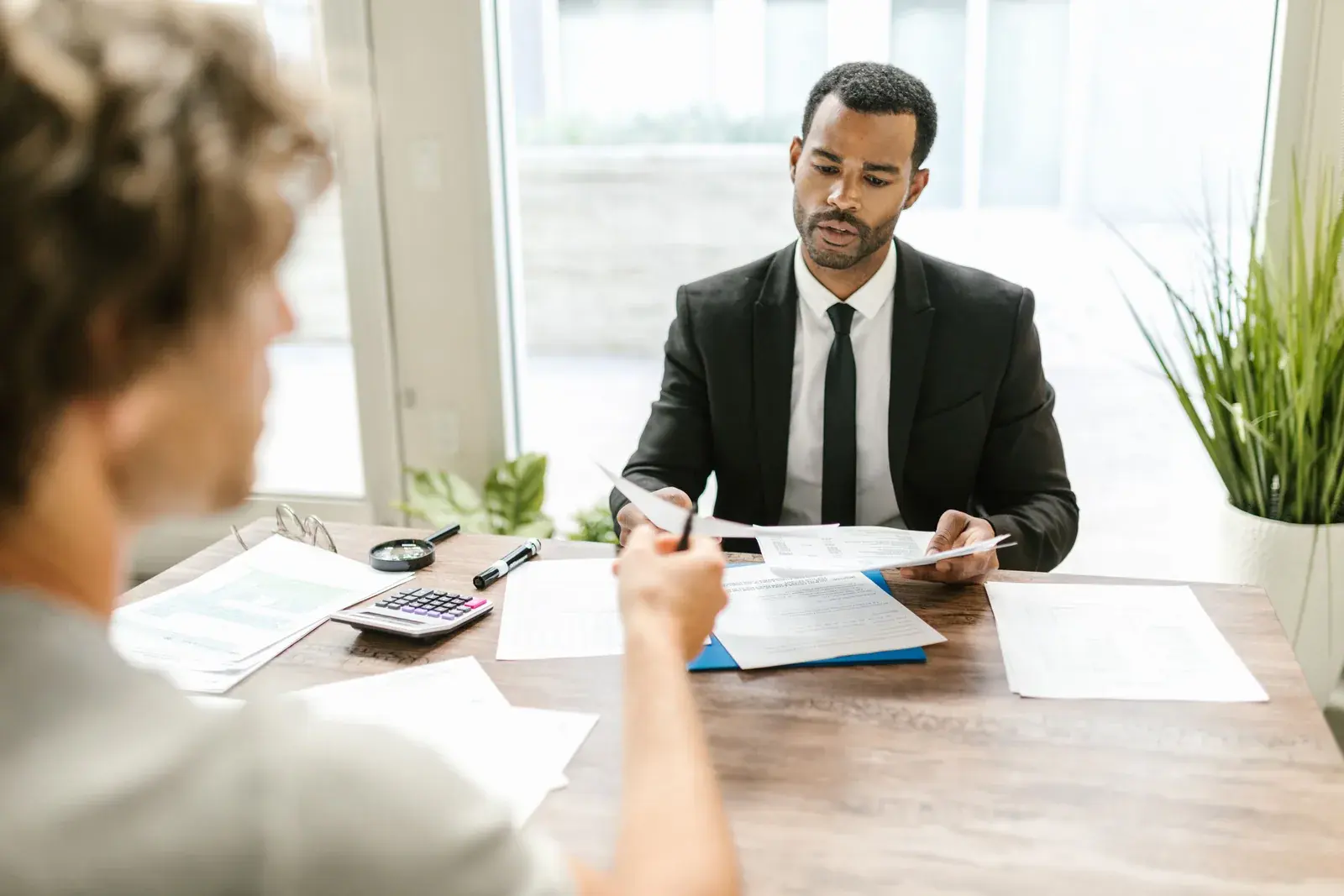 A tax professional in a dark blazer reviews a client folder at a wood desk with a laptop and a cup of coffee