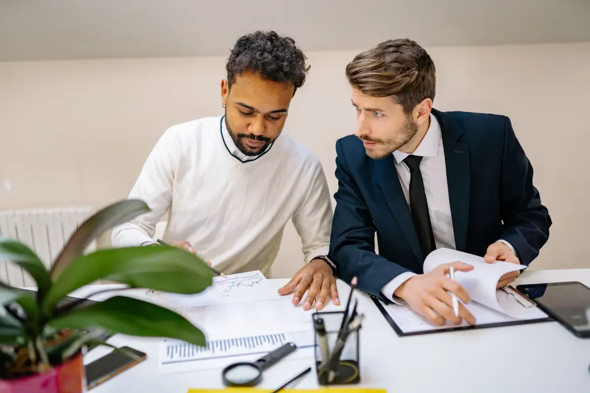 Two people at a desk lean over printed charts and a clipboard, talking through the figures together.