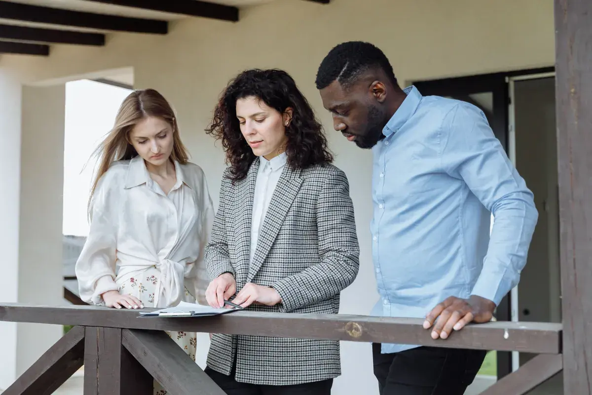 Three adults standing on a home terrace reviewing paperwork on a clipboard together
