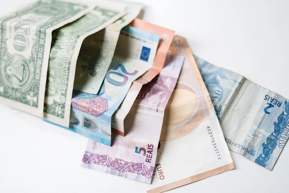 Banknotes from several countries fanned out on a white surface