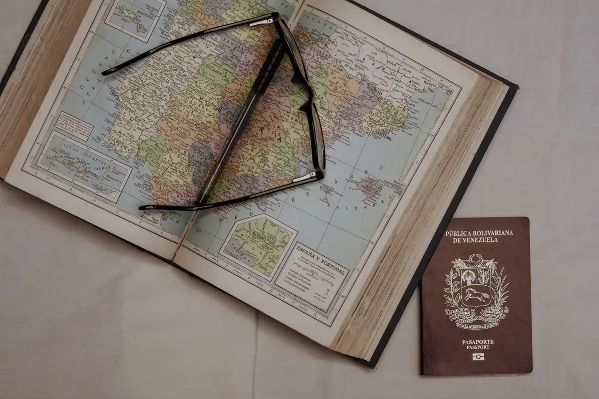 An open atlas with reading glasses beside a passport on a linen surface
