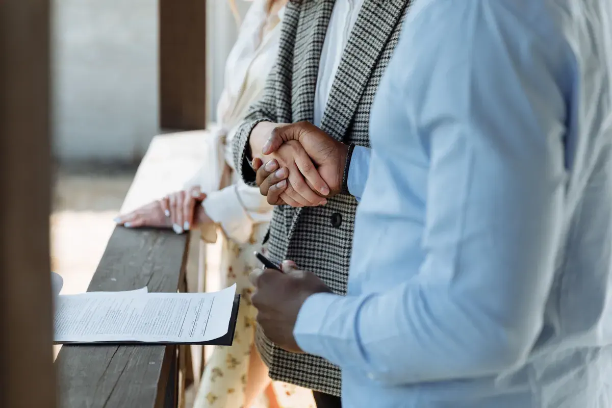 Two people shake hands over a signed property agreement resting on a wooden ledge