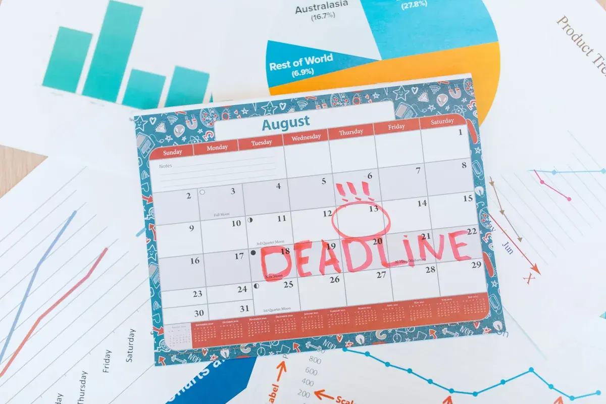 A monthly wall calendar with a word written in bold red marker across a circled date, resting on printed business charts