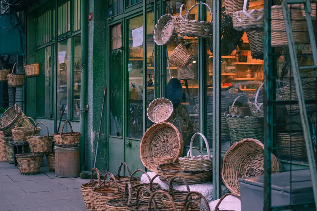 Woven baskets and other goods displayed for sale outside the glass front of a small shop.
