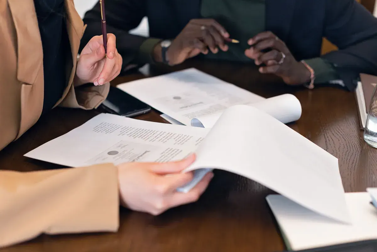Two professionals review printed documents together across a dark wooden table.