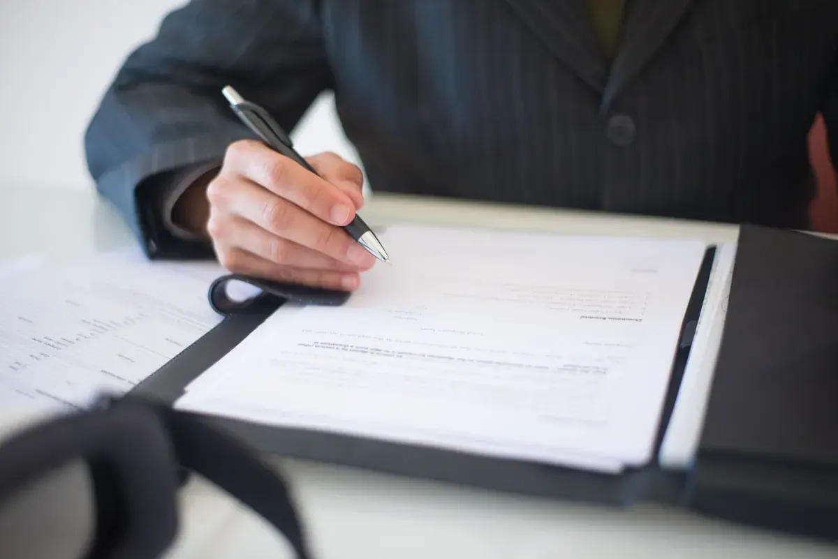 A person in a suit fills out a printed form held open in a black binder.