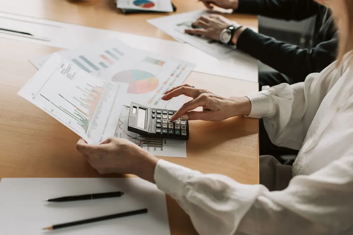Dos personas en una mesa de reunión revisan gráficos impresos mientras una usa una calculadora.