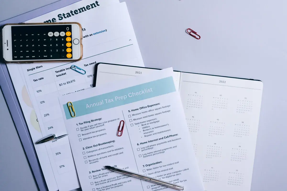 Vista cenital de una lista de preparación de impuestos, estados impresos, una calculadora y páginas de calendario.