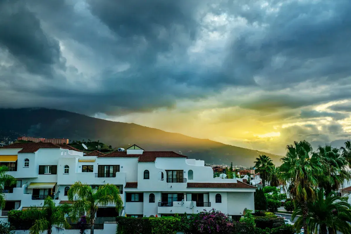 A row of tropical homes with lush palms backlit by a vibrant sunset and dramatic clouds