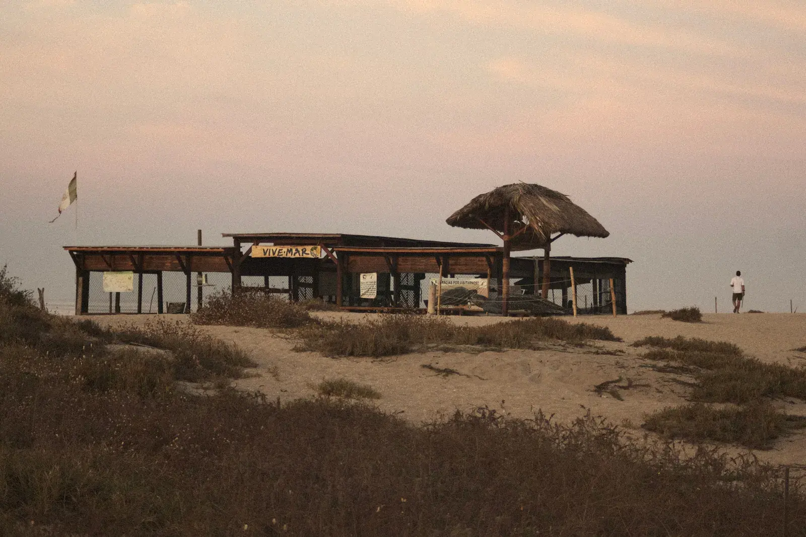 A rustic beach hut on a quiet Mexican coastline at dusk with dramatic clouds overhead and warm light