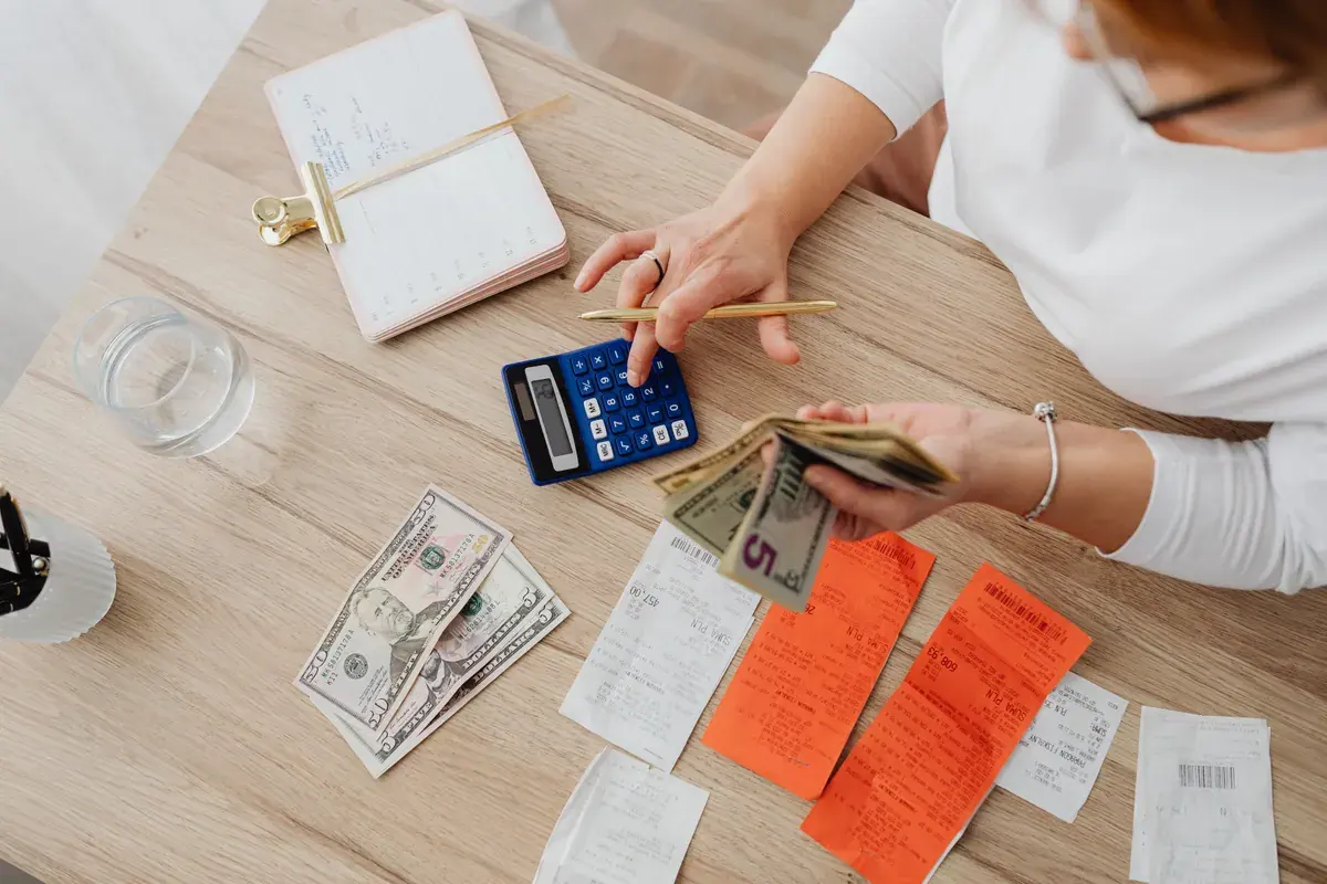 Overhead view of a desk with paper receipts, a calculator, a notebook and cash in hand.