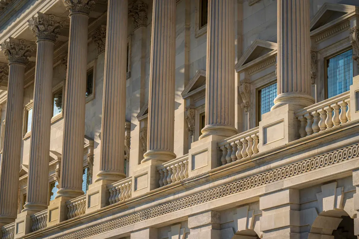 Tall classical stone columns on a government building facade lit by warm late day sun.