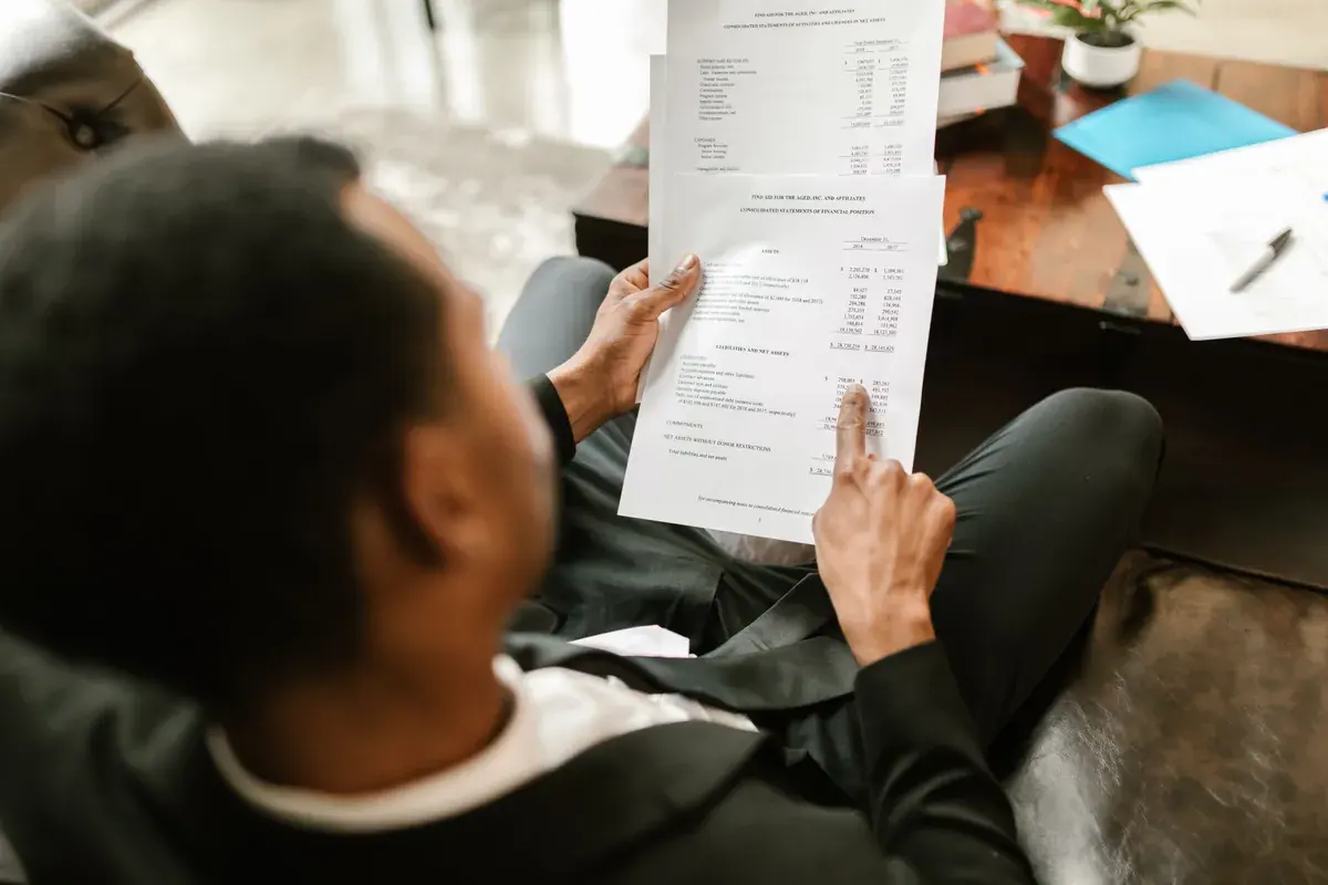 A business professional seated with a printed financial statement, tracing a line on the page with a finger