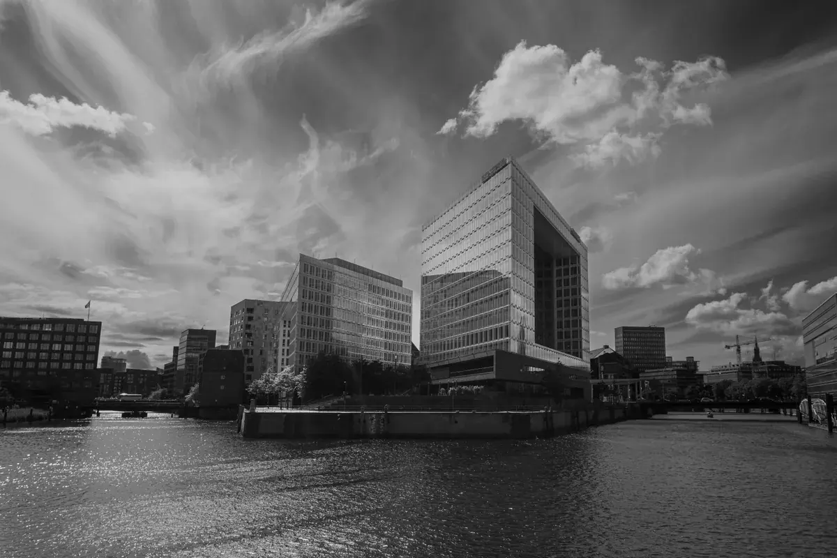 A modern office building on a waterfront under an overcast sky, in black and white